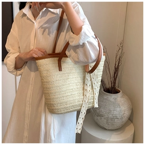 Detail of woven straw tote bag with brown leather handles and decorative lace ribbon