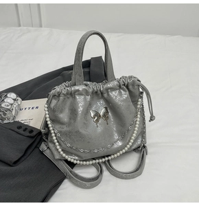 Detalle de mochila plateada metalizada con mariposa y cadena decorativa de perlas
