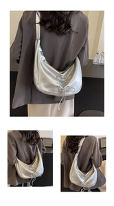 Close-up of metallic silver crescent bag featuring decorative bows and wide strap detail