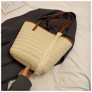 Close-up of woven straw tote bag with brown leather handles and white lace detail