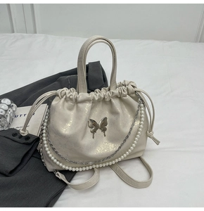 Detalle de bolso blanco perla con cordón, mariposa plateada y adorno de cadena de perlas