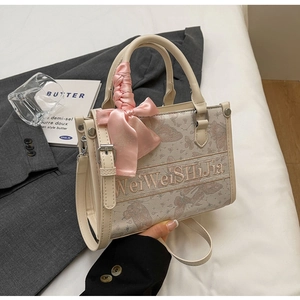 Detail einer cremefarbenen Handtasche mit rosa Schmetterlingsstickerei und Satin-Schleife