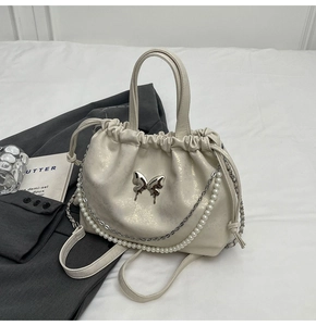 Detalle de bolso crema mariposa con cadena de perlas y hebilla plateada brillante