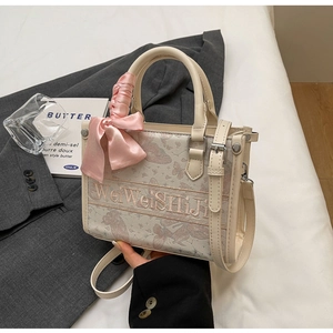 Detail der cremefarbenen Handtasche mit rosa Schmetterlingsstickerei und edler Seidenschleife