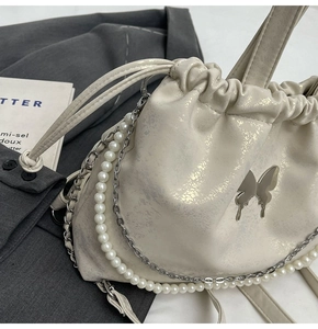 Detalle del bolso de hombro mariposa crema con cadena de perlas sobre chaqueta