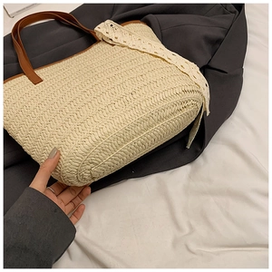 Detail of beige woven straw tote bag featuring white lace ribbon and brown leather straps