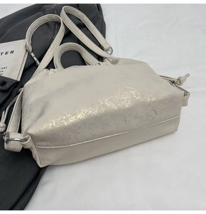 Detalle de bolso blanco crema con acabado texturizado y nudo de cordón en el lateral