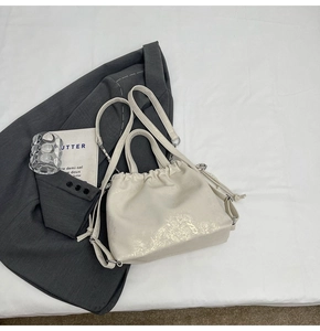 Detalle del bolso de mano blanco con purpurina, cierre de cordón y herrajes plateados
