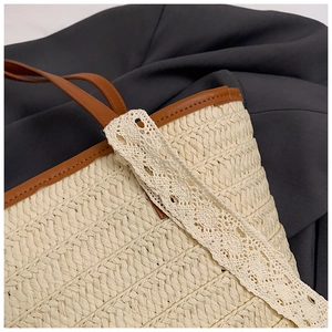 Detail of woven straw tote bag with brown leather trim and delicate white lace texture