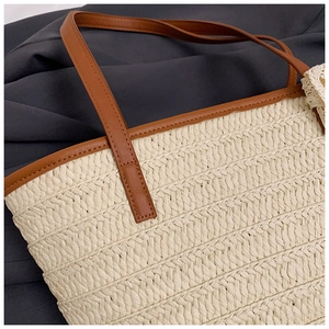 Detail of woven straw tote bag with brown leather handles and fine stitching texture