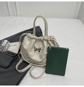 Detalle de bolso saco de cuero sintético crema con cadena de perlas y mariposa metálica