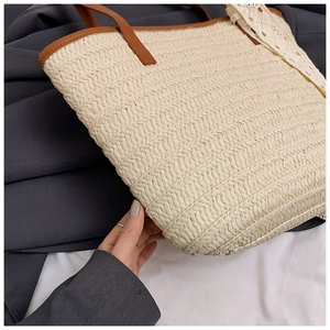 Detail of woven straw tote bag featuring white lace trim and brown leather handles