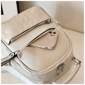 Close-up of cream faux leather backpack showing quilted flap and smartphone storage capacity