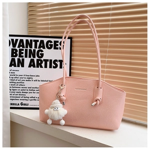 Détail d'un sac cabas rose avec plis souples, logo de mode et pendentif peluche blanc