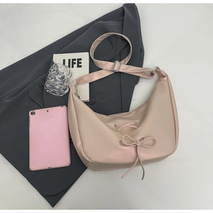 Detail of pink dumpling bag featuring a ribbon bow and adjustable strap in lifestyle setting