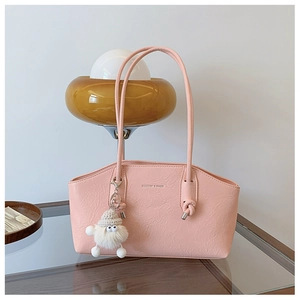 Détail du sac sous le bras en cuir gaufré rose avec logo doré et breloque en peluche