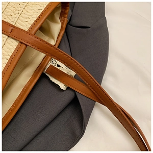 Close-up of woven straw bag showing white lace edge and brown leather shoulder strap