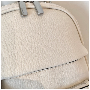 Close-up of litchi pattern faux leather and silver zipper detail on cream backpack