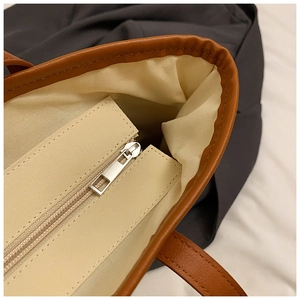 Detail of woven tote bag showing canvas lining, metal zipper and brown leather trim