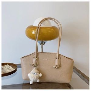Détail du sac à bandoulière beige montrant la texture plissée et le pendentif en peluche