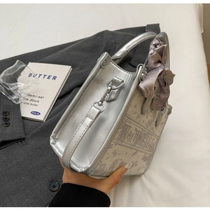 Seitenansicht der silbernen Metallic-Handtasche mit Doppelgriffen und grauem Satin-Anhänger