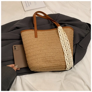 Detail of woven straw tote bag featuring brown leather handles and delicate white lace trim