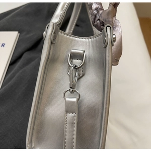 Detailansicht einer silbernen Handtasche mit silbernem Karabiner und floralem Seidentuch am Griff