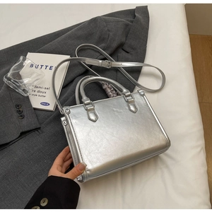 Draufsicht einer metallic-silbernen Handtasche mit Doppelgriffen und Schultergurt