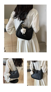 Detail of black leather underarm bag with gold logo lettering and a plush sheep charm