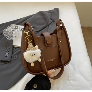 Close-up of brown leather bucket bag with gold lettering and white sheep plush charm