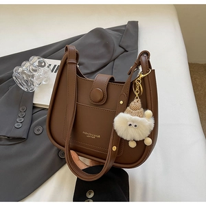 Detail of brown leather tote bag featuring gold lettering and cute white plush charm