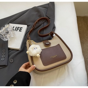 Detail of hobo shoulder bag in beige and brown contrast with a cute plush monster charm