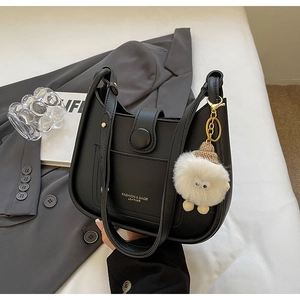 Detail of black leather bucket bag with gold lettering and cute plush charm accessory