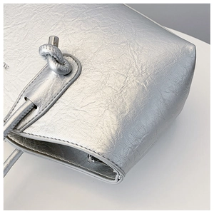 Détail d'un sac argenté métallisé avec nœud décoratif et fermeture éclair en métal brillant