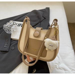 Detail of beige and brown bucket bag with gold logo and plush keychain charm