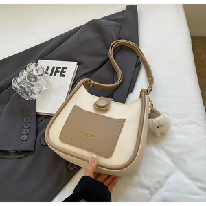 Close-up of cream and khaki bucket bag with plush charm on a minimal bed setting
