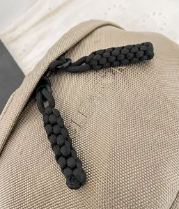 Macro shot of double zippers with black woven pull cords on a khaki canvas cross-body bag
