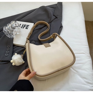 Detail of minimalist cream leather hobo bag with brown strap and plush charm