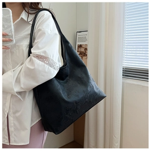 Detail of black large hobo bag with floral embossed texture worn by a model