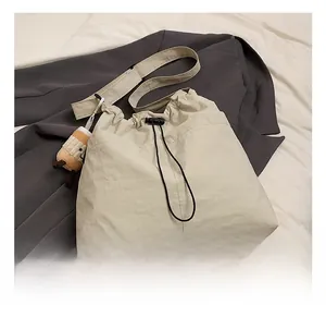 Detail view of cream nylon drawstring tote bag with plush charm and wide strap