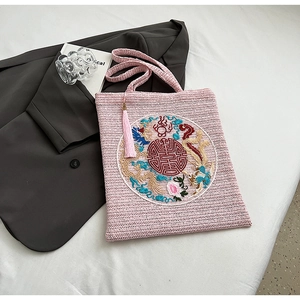 Detailed embroidery of a golden dragon on a pink woven tote bag with a fringe tassel