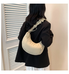 Rear view of a beige pleated crescent shoulder bag with ruffle strap on a black blazer