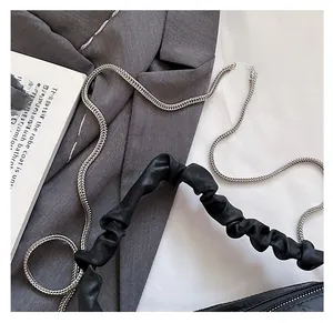 Detail of black pleated shoulder strap with silver metal chain on a stylish handbag