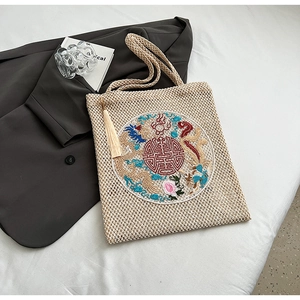 Close-up of beige woven tote bag featuring traditional Chinese embroidery and tassel detail