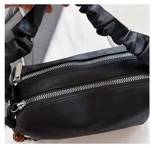 Detail of smooth silver double zippers on black pleated handle bag with chain