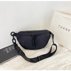 Detail of black canvas crossbody bag with chain strap on a white lace fabric background