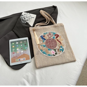 Detail of hand-woven beige tote bag with traditional Chinese dragon embroidery and tassels
