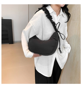 Detail of black crescent shoulder bag with pleated strap and side bow decoration