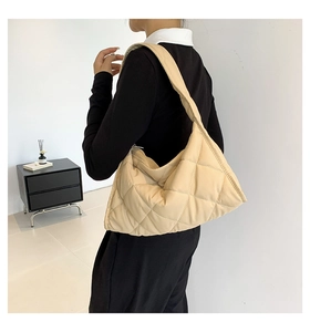 Modelo luciendo un bolso hobo acolchado beige en un interior minimalista, vista lateral