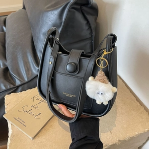 Black leather bucket bag for women with gold lettering and plush charm on stone base